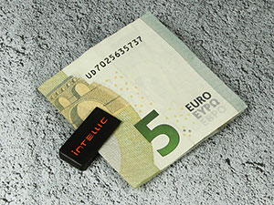 USB-Stick neben einem 5-Euro-Schein auf einer grauen Oberfläche, ideal für Werbezwecke mit individuellem Branding.